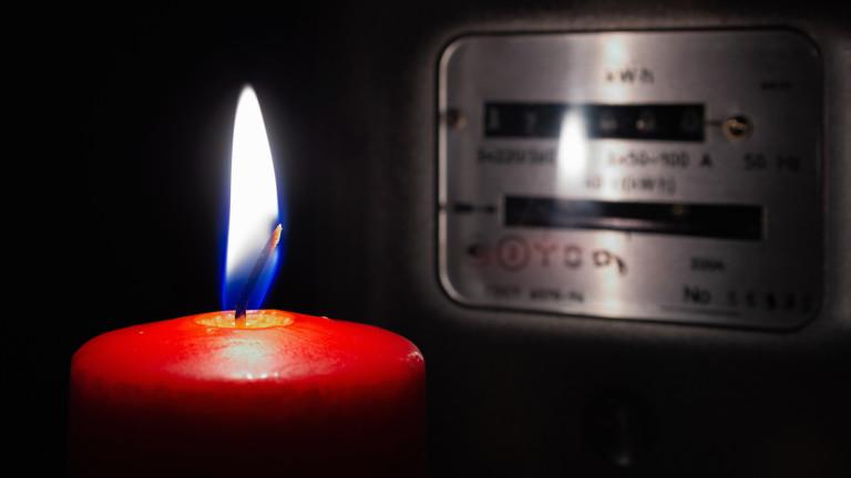 Candle is lit in the dark near electricity meter at home.